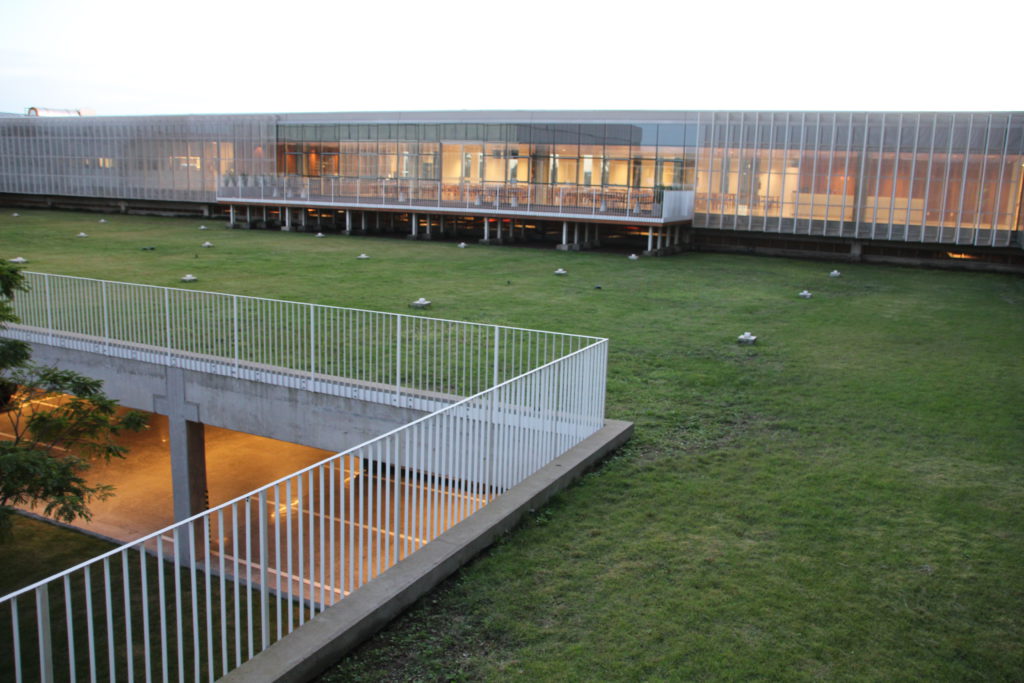 Cobertura ajardinada em edifício institucional com cercas metálicas brancas e fachada envidraçada, representando aplicação de telhado verde em edifícios públicos ou corporativos.