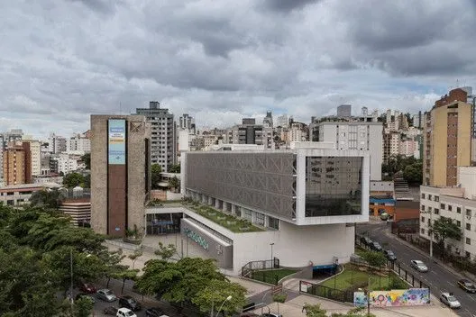 Vista panorâmica de um edifício corporativo moderno e sustentável no centro de uma cidade. O prédio possui múltiplas áreas de telhado verde e vegetação em sua estrutura, além de amplas janelas para iluminação natural, demonstrando o uso de tecnologias de infraestrutura verde para eficiência operacional e certificações ambientais.