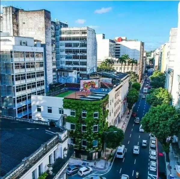 Vista urbana de um edifício de esquina com uma densa fachada de jardim vertical e telhado verde. A imagem ilustra a transformação de um ativo urbano através da sustentabilidade imobiliária para reduzir o Brown Discount.
