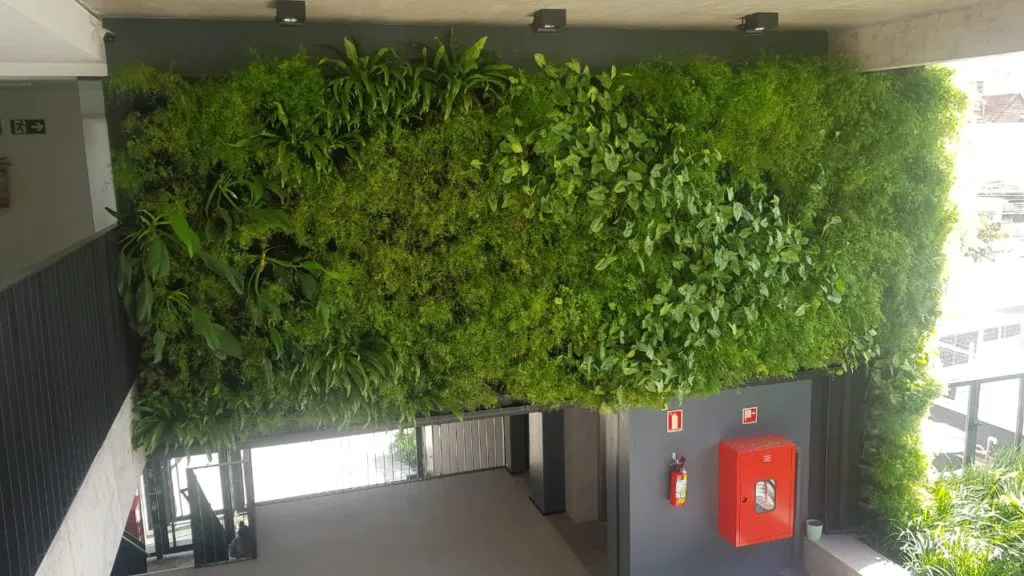 Parede interna de um prédio corporativo com o Jardim Vertical Mamute da Ecotelhado. A vegetação densa promove bem-estar e retenção de inquilinos, transformando o hall de entrada em um ambiente de alta performance humana.