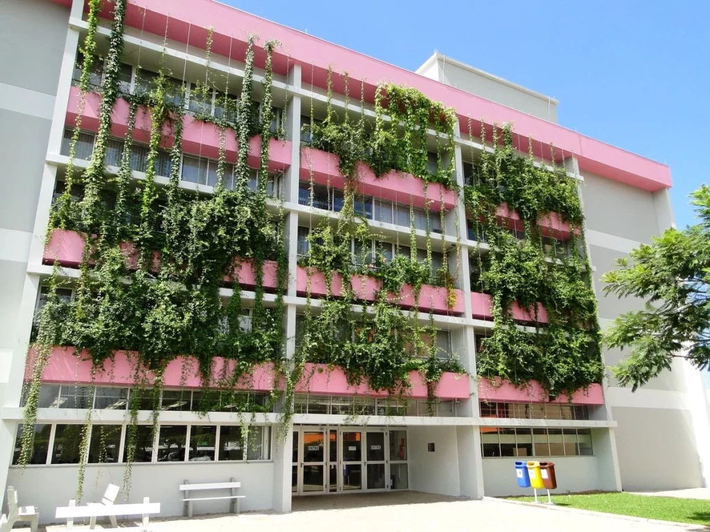 A imagem mostra um prédio universitário nas cores branco e rosa com brises verticais se estendendo na fachada, criando uma atmosfera que harmoniza o urbano com o natural.