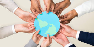 imagem várias mãos unidas segurando uma imagem do planeta simbolizando a sustentabilidade em ambientes corporativos