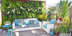 Imagem de dois sofás brancos listrados com almofadas azuis, com fundo de jardim vertical para simbolizar um projeto de paisagismo
