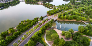 Vista aérea de um grande parque urbano com lagos, árvores densas e vias arborizadas, ilustrando o conceito de cidades esponja, onde áreas verdes e corpos d’água ajudam a absorver e gerenciar a água da chuva de forma natural.
