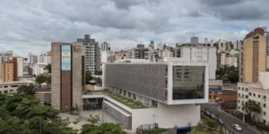 Vista panorâmica de um edifício corporativo moderno e sustentável no centro de uma cidade. O prédio possui múltiplas áreas de telhado verde e vegetação em sua estrutura, além de amplas janelas para iluminação natural, demonstrando o uso de tecnologias de infraestrutura verde para eficiência operacional e certificações ambientais.