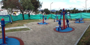 Área de playground e academia ao ar livre em condomínio, destacando o ecopavimento no chão e os equipamentos coloridos de ginástica instalados sobre círculos emborrachados.