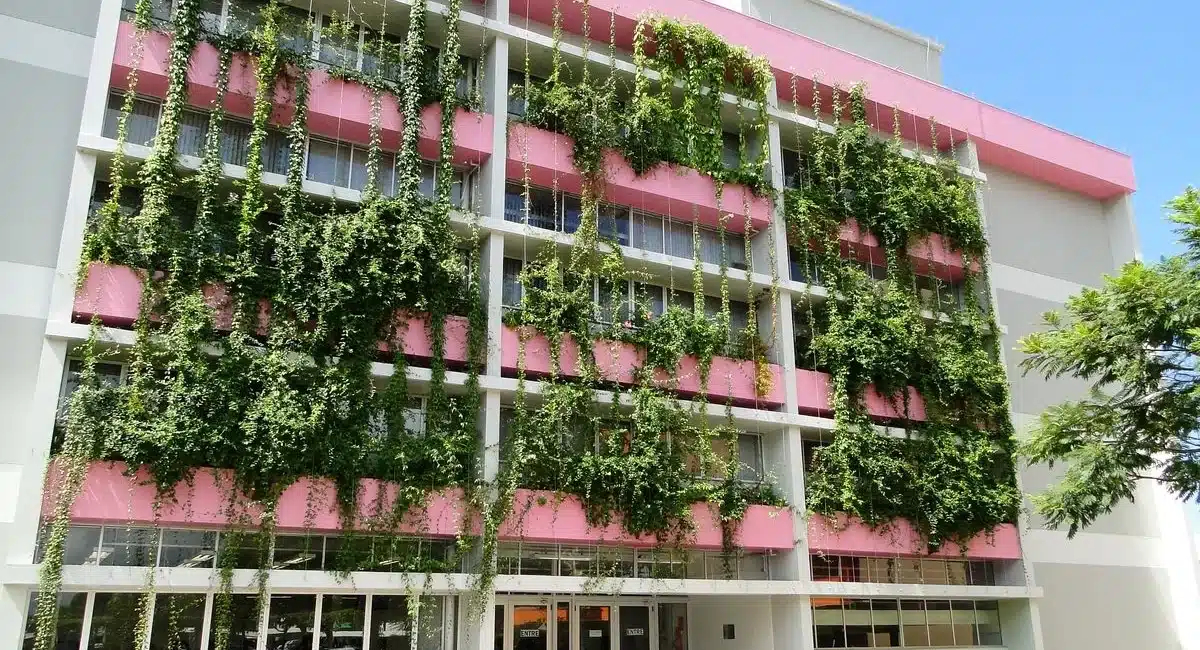 A imagem mostra um prédio universitário nas cores branco e rosa com brises verticais se estendendo na fachada, criando uma atmosfera que harmoniza o urbano com o natural.