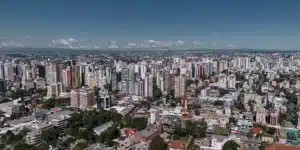 Vista aérea da cidade de Curitiba no Paraná, com seus grandes blocos de apartamentos e um céu azul com poucas nuvens ao fundo.